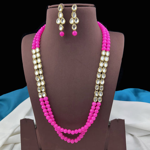 Pink beaded necklace with gold accents and matching earrings on a brown stand.