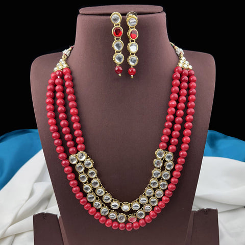 Jewelry set with red beaded necklace and earrings on a brown stand.