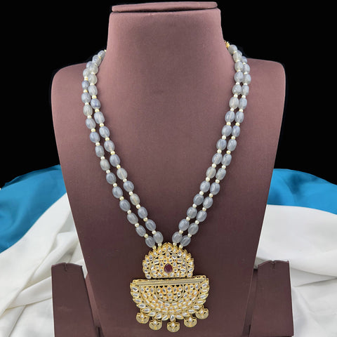 Beaded necklace with a gold pendant on a brown stand against a white and blue fabric background