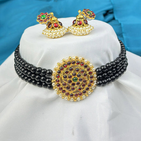 Black beaded necklace with gold and multicolor pendant on a white cushion, blue background