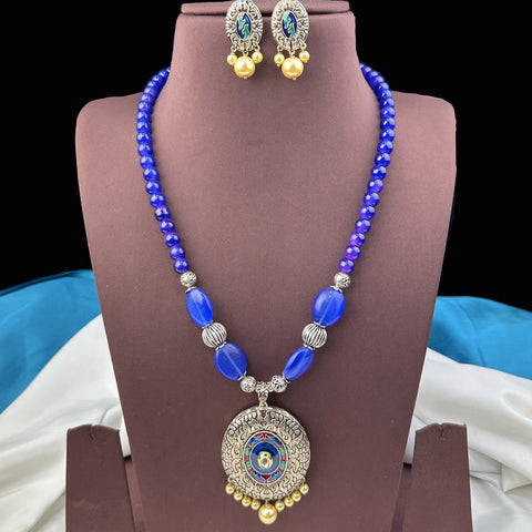 Blue beaded necklace with a pendant and matching earrings on a brown stand.