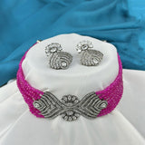 Jewelry set with pink beaded necklace and silver earrings on a white stand against a blue fabric background.