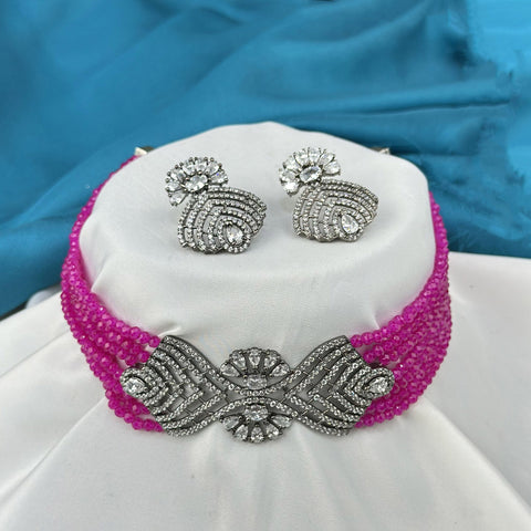 Jewelry set with pink beaded necklace and silver earrings on a white stand against a blue fabric background.