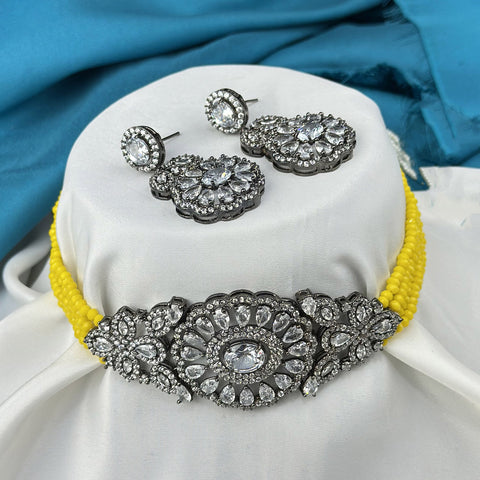 Jewelry set with a yellow choker and matching earrings on a white cushion with blue fabric background