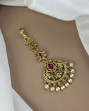 Decorative gold pendant with pearls and gemstones on a white fabric background