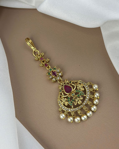 Decorative gold pendant with pearls and gemstones on a white fabric background