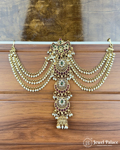 Ornate gold necklace with red and green stones on a wooden surface, brand 'Jewel Palace' visible.