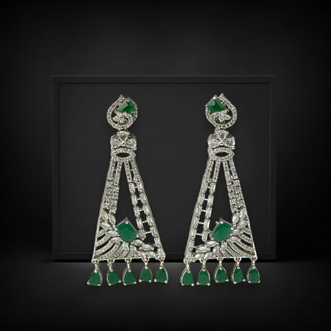 Pair of ornate earrings with green gemstones on a black background