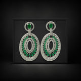 Pair of earrings with green gemstones and silver accents on a black background