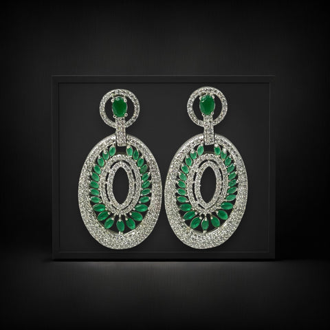 Pair of earrings with green gemstones and silver accents on a black background