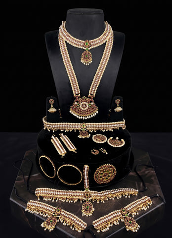 A gold and cream jewelry set displayed on a black mannequin bust and stand, including a necklace, earrings, bracelets, rings, and a choker, with matching pieces arranged on a marble surface against a black background.