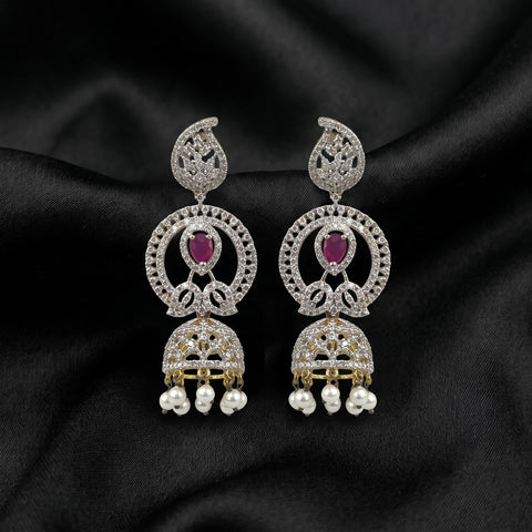 A pair of ornate Indian jhumka earrings with silver-toned metal, clear pavé stones, oval ruby gemstones, and dangling pearl-like beads, displayed on a black satin fabric background.