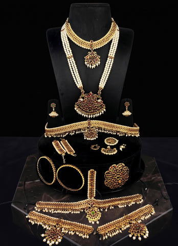 A traditional Indian gold and pearl jewelry set displayed on a black velvet mannequin bust and stand. The set includes a high-neck necklace, a long chain with a large pendant, a choker, earrings, bangles, a necklace plate, and a waist chain, all decorated with gold and white pearls.