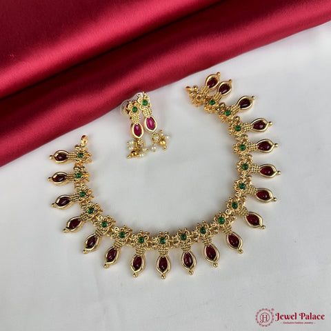 Gold necklace and earrings with red and green stones on a white surface with red fabric background