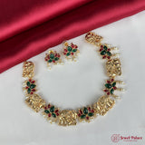 Gold necklace with green and red stones on a white surface with a red fabric background