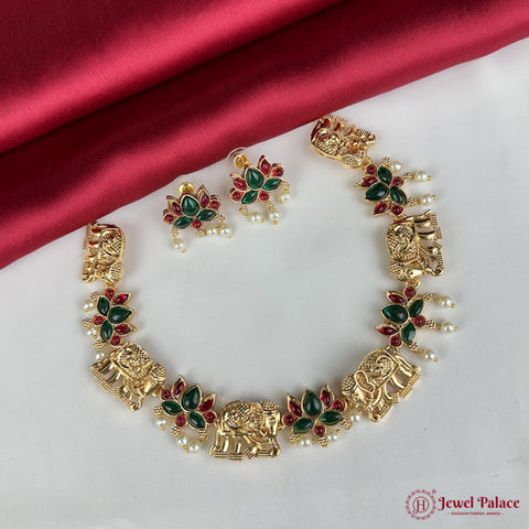 Gold necklace with green and red stones on a white surface with a red fabric background