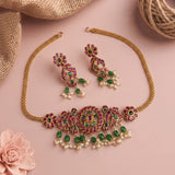 Gold-plated jewelry set featuring a necklace and matching earrings adorned with pink stones, green stones, and white faux pearls, styled on a pink background with burlap and a flower prop.