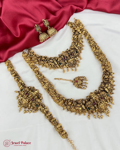 Gold jewelry set including necklace, earrings, and bangles on a white and red fabric background.