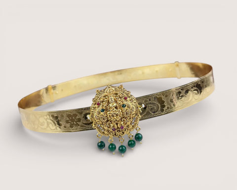 Gold belt with decorative clasp and green gemstones on a light gray background