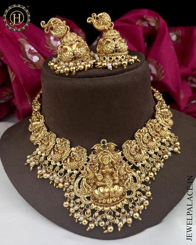 Gold plated kemp stone temple necklace with earrings, displayed on a brown mannequin, with red and gold floral patterned fabric in the background.