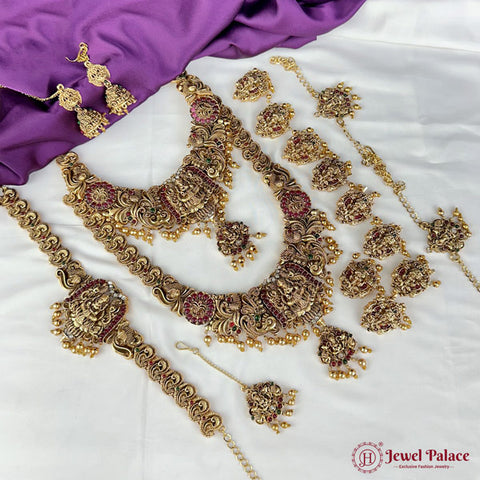 Gold jewelry set with necklaces, earrings, and other accessories on a white and purple fabric background.