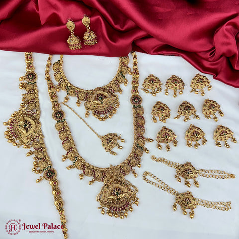 Gold jewelry set including necklaces, earrings, and bangles on a red fabric background.