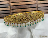 Gold tiara with green and red stones on a white fabric background
