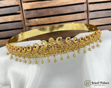 Gold tiara with intricate designs and red stones on a white surface with wooden background