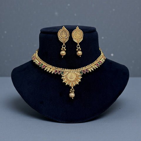 Gold necklace and earrings set on a black velvet stand with a gray background