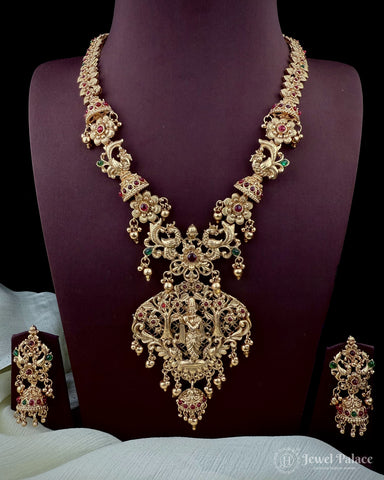 Ornate gold necklace with gemstones on a mannequin bust, accompanied by matching earrings.