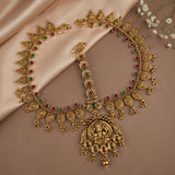Gold-toned traditional Indian jewelry set featuring a necklace with a large deity pendant, a matching bracelet, and a collar, decorated with red and green stone accents, displayed on beige satin fabric.