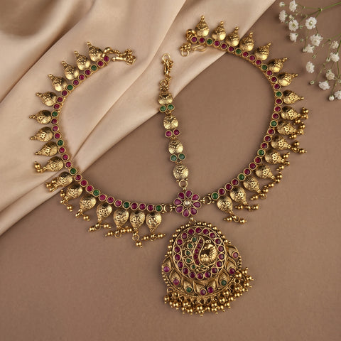 Gold-toned Indian Kundan necklace set with a matching necklace and pendant, decorated with red and green stones, displayed on a beige satin fabric background.