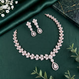 A rose gold jewelry set featuring a necklace and matching earrings, decorated with sparkling clear stones in a leaf and teardrop motif, displayed on a dark green satin fabric background.