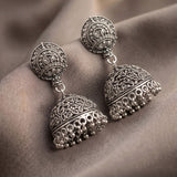 A pair of ornate silver-toned Indian jhumka earrings with intricate filigree detailing and dangling bead tassels, displayed on draped taupe fabric.