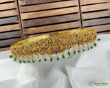 Gold tiara with green and red gemstones on a white fabric background