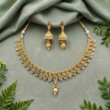 Gold-toned traditional Indian jewelry set featuring a necklace and matching earrings, decorated with small multicolored stones and bead details, arranged on a sage green fabric background with decorative green leaves.
