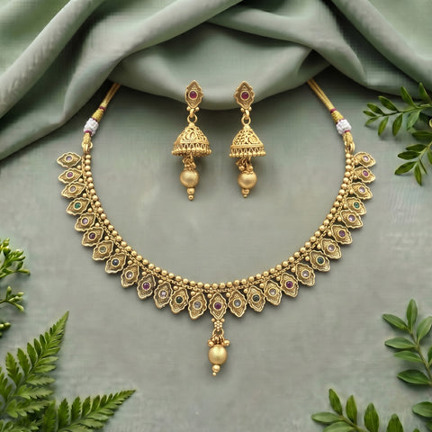 Gold-toned traditional Indian jewelry set featuring a necklace and matching earrings, decorated with small multicolored stones and bead details, arranged on a sage green fabric background with decorative green leaves.