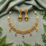 Gold-toned traditional jewelry set with a necklace and matching earrings, decorated with small red and green stones and white pearl-like beads, arranged on a soft sage green fabric with green leaves around it.