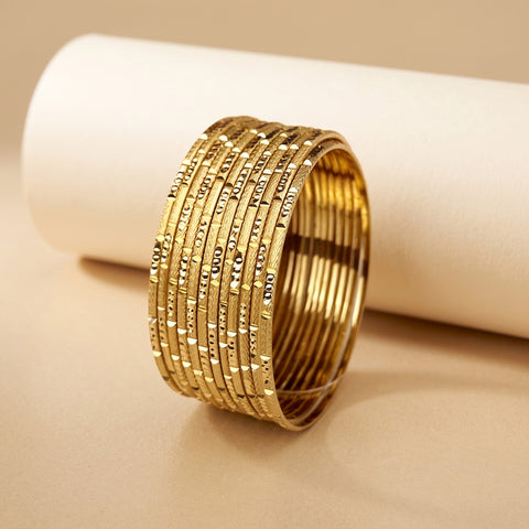 A stack of gold-plated bangles with engraved numbers, displayed on a beige surface with a white cylindrical prop.