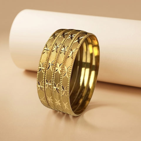 A wide gold bangle bracelet with three parallel bands, featuring textured star patterns and beaded borders, displayed on a beige surface with a white cylindrical prop.