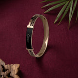 A rose gold bangle bracelet with a black enamel inlay featuring the Cartier logo, displayed on draped white fabric.