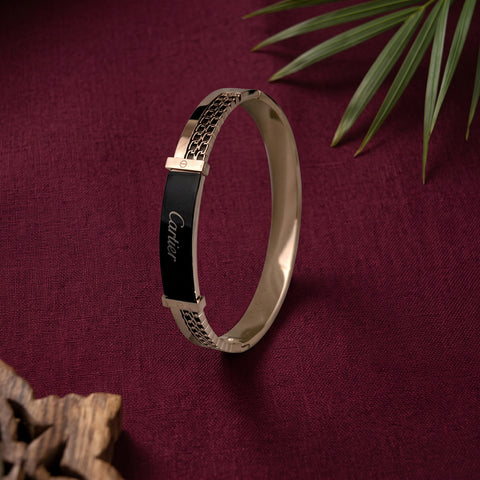 A rose gold bangle bracelet with a black enamel inlay featuring the Cartier logo, displayed on draped white fabric.