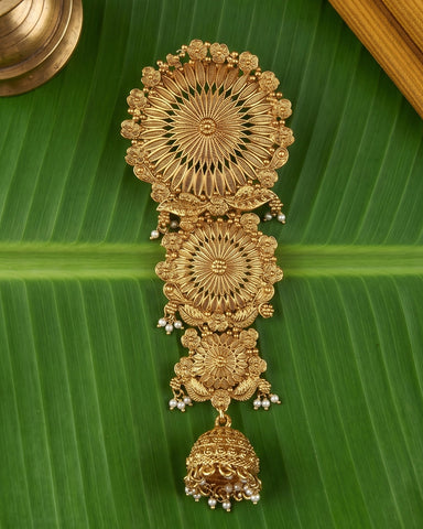 An ornate gold-toned traditional Indian jewelry piece with intricate filigree patterns and small pearl-like bead accents, displayed on a large green banana leaf.