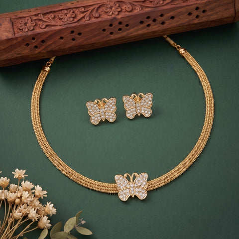 Gold-tone butterfly jewelry set with a matching necklace and earrings, featuring pavé-set clear stones, displayed on a dark green background with a carved wooden prop and small dried flowers.