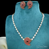 Pearl necklace with red gemstone pendant and matching earrings on a teal stand.