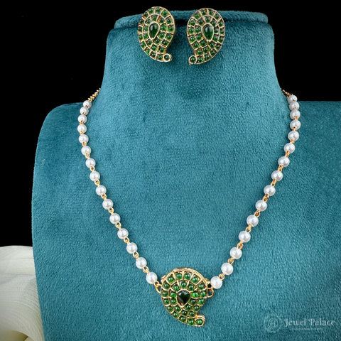 Pearl necklace with green gemstone pendant and matching earrings on a teal stand, brand 'Jewel Palace' visible.