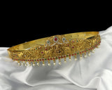 Gold tiara with red and green gemstones on a white fabric background