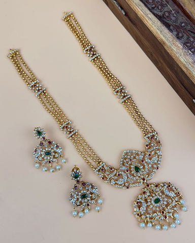 Ornate gold necklace with gemstones on a light pink surface