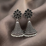 A pair of silver-toned Indian jhumka earrings with black stone accents in the floral tops and a row of small white pearl-like beads along the bottom, displayed on draped taupe fabric.