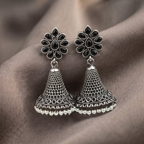 A pair of silver-toned Indian jhumka earrings with black stone accents in the floral tops and a row of small white pearl-like beads along the bottom, displayed on draped taupe fabric.